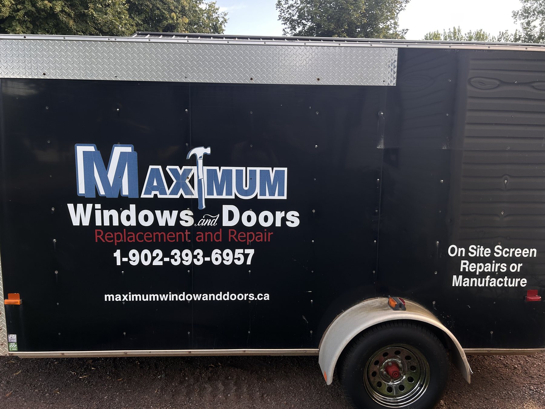 The black Maximum Windows & Doors work trailer with the company decal: name, phone number, website, replacement and repair, on site screen repairs or manufacture